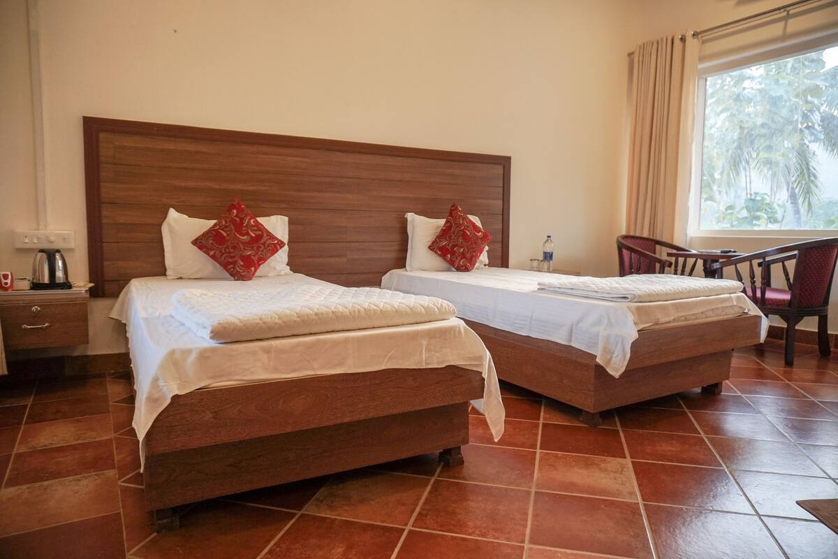 Een hotelkamer met twee bedden, een houten hoofdeinde, een stoel en een raam met gordijnen.