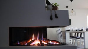 Et moderne køkken med indbygget pejs, et spiseområde med stole og en hængende lampe.
