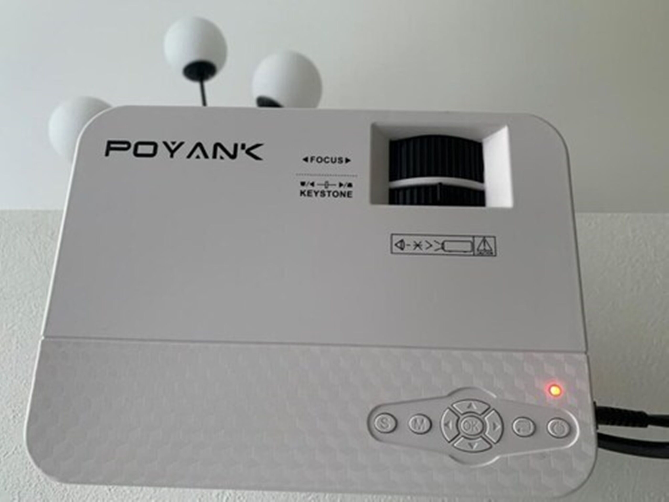 Dispositivo electrónico blanco con el nombre de marca 'POYAN' y modelo 'FOCUS' a la vista. Tiene un botón de encendido, una luz indicadora roja y un símbolo de batería.