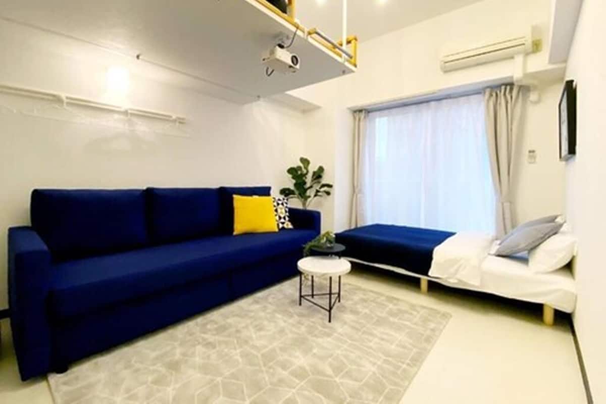 Ein modernes Wohnzimmer mit einem blauen Sofa, einem kleinen runden Tisch und einem Fenster mit Vorhängen.