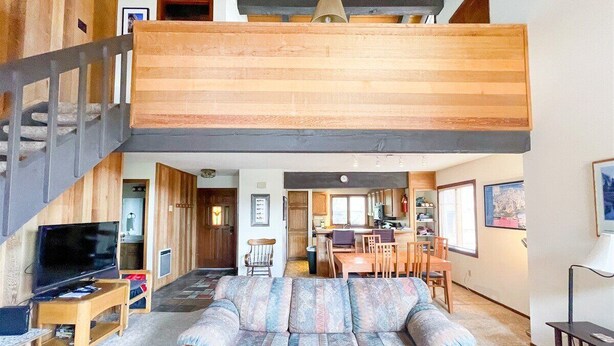 A spacious living area with a large couch, a television, and a staircase leading to an upper level.