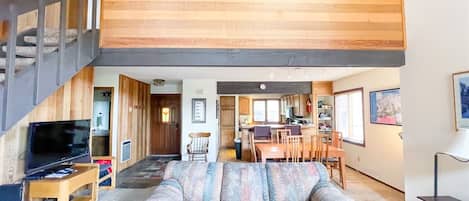 Cozy living area with a comfortable sofa, dining table, and TV, leading to a staircase.