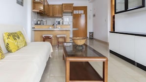 A compact living space with a sofa, a dining table, a kitchen area, and a TV mounted on the wall. - Turquesa by Interhome (La Pineda)