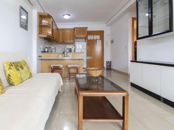 A compact living space with a sofa, a dining table, a kitchen area, and a TV mounted on the wall.