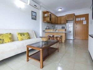A compact living space with a kitchenette, a sofa with yellow cushions, and a glass-top table.