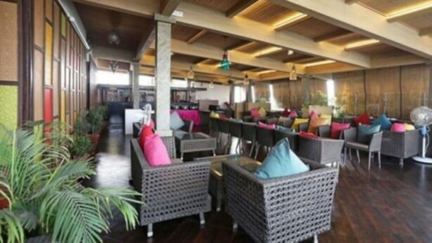 A spacious indoor area with wicker furniture, a long counter, and potted plants. - Gulabi Bagh Resort (A unit of Sarvmangla Garden) (Jaipur)