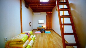 A narrow room with wooden flooring, a bed with colorful bedding, a small table with a television, and a wooden ladder. - Jeonju Happy Maru Hanok (Jeonju)
