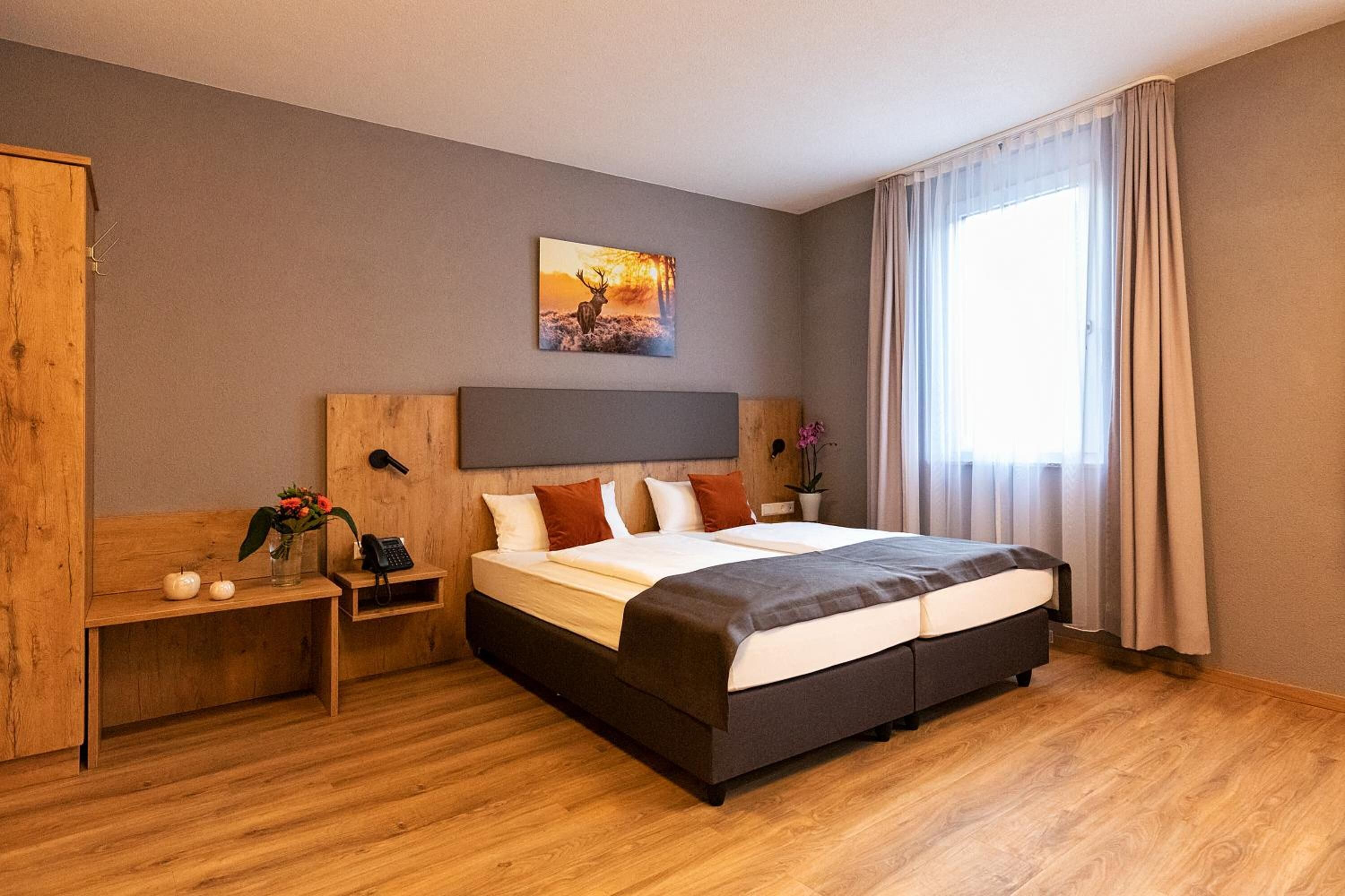 Une chambre d’hôtel moderne avec un grand lit, une tête de lit en bois, une table de chevet avec une lampe et un tableau au mur.