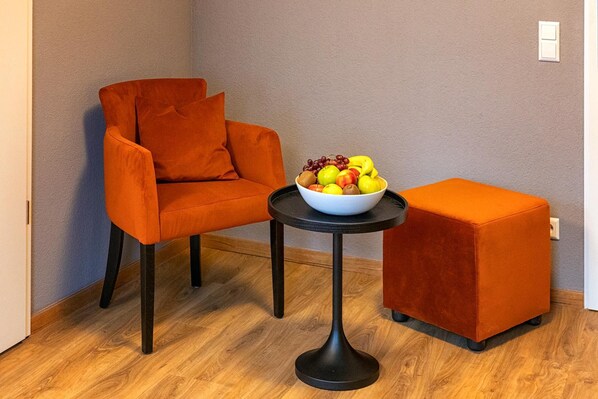 A modern room with an orange armchair, a small round table with a bowl of fruit, and a matching ottoman.