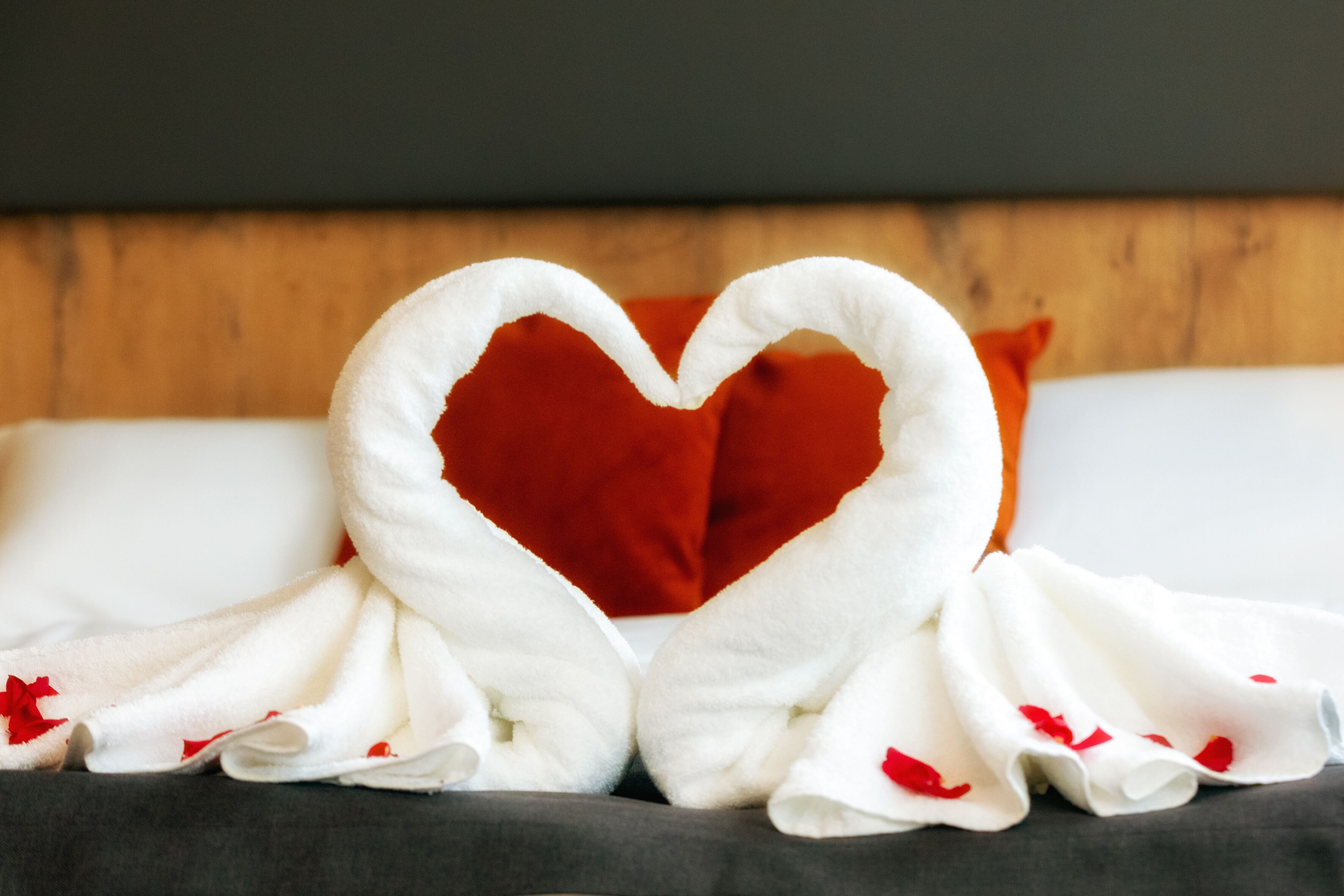 A bed with a heart-shaped towel arrangement and a red pillow.