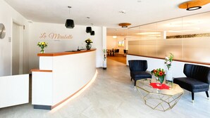 Zona de recepción de un hotel con un mostrador curvo, dos sillones tapizados negros, una mesa de centro de cristal y un jarrón con flores.