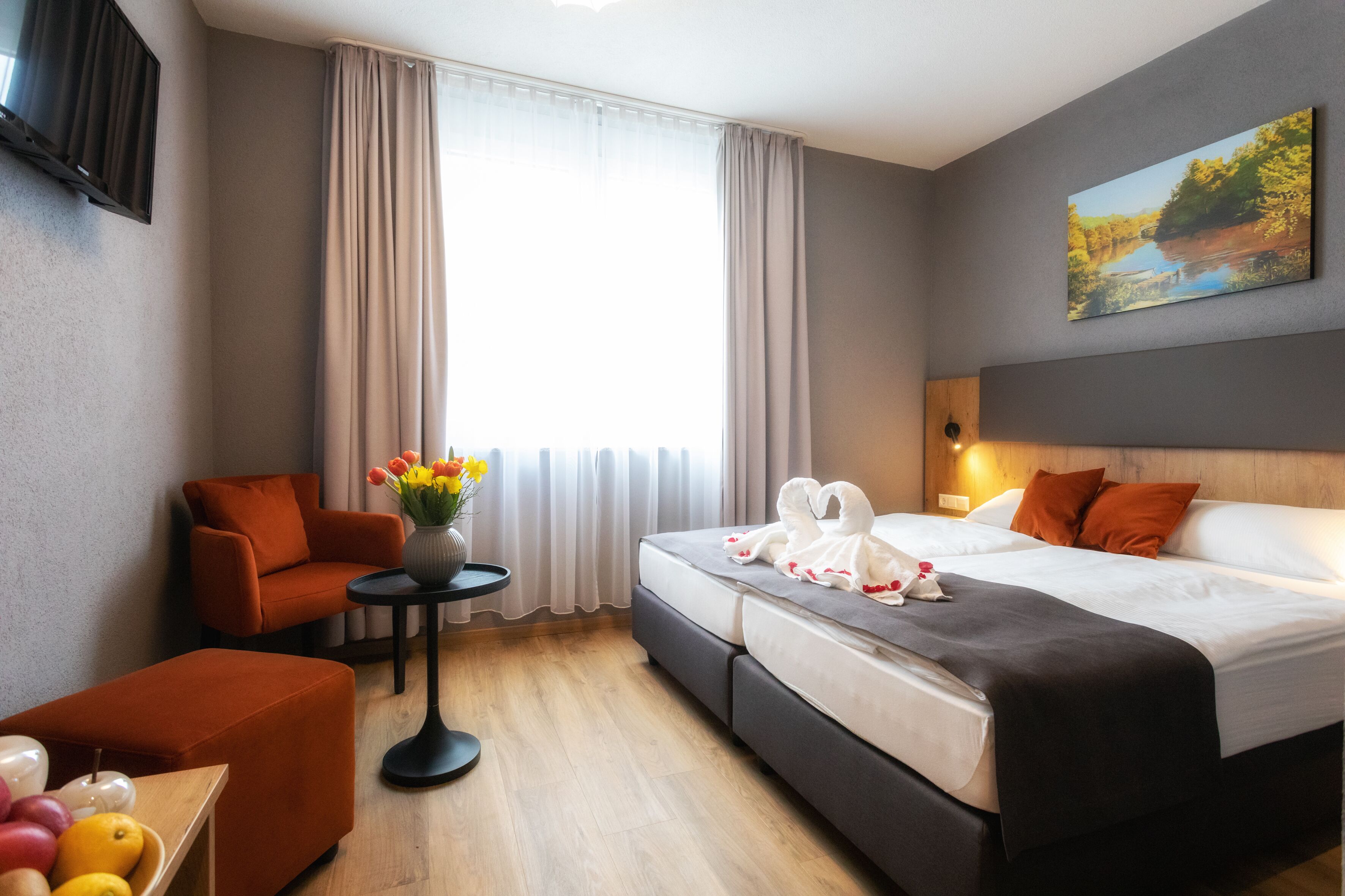 Une chambre d’hôtel moderne, avec un lit, un canapé, une petite table ornée d’un vase de fleurs et un tableau accroché au mur.