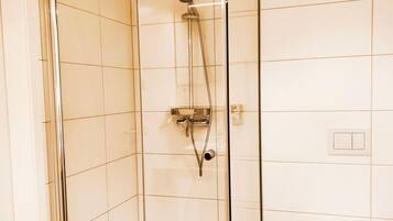 A glass-enclosed shower with a handheld showerhead, a wall-mounted control panel, and a toilet in a tiled bathroom.