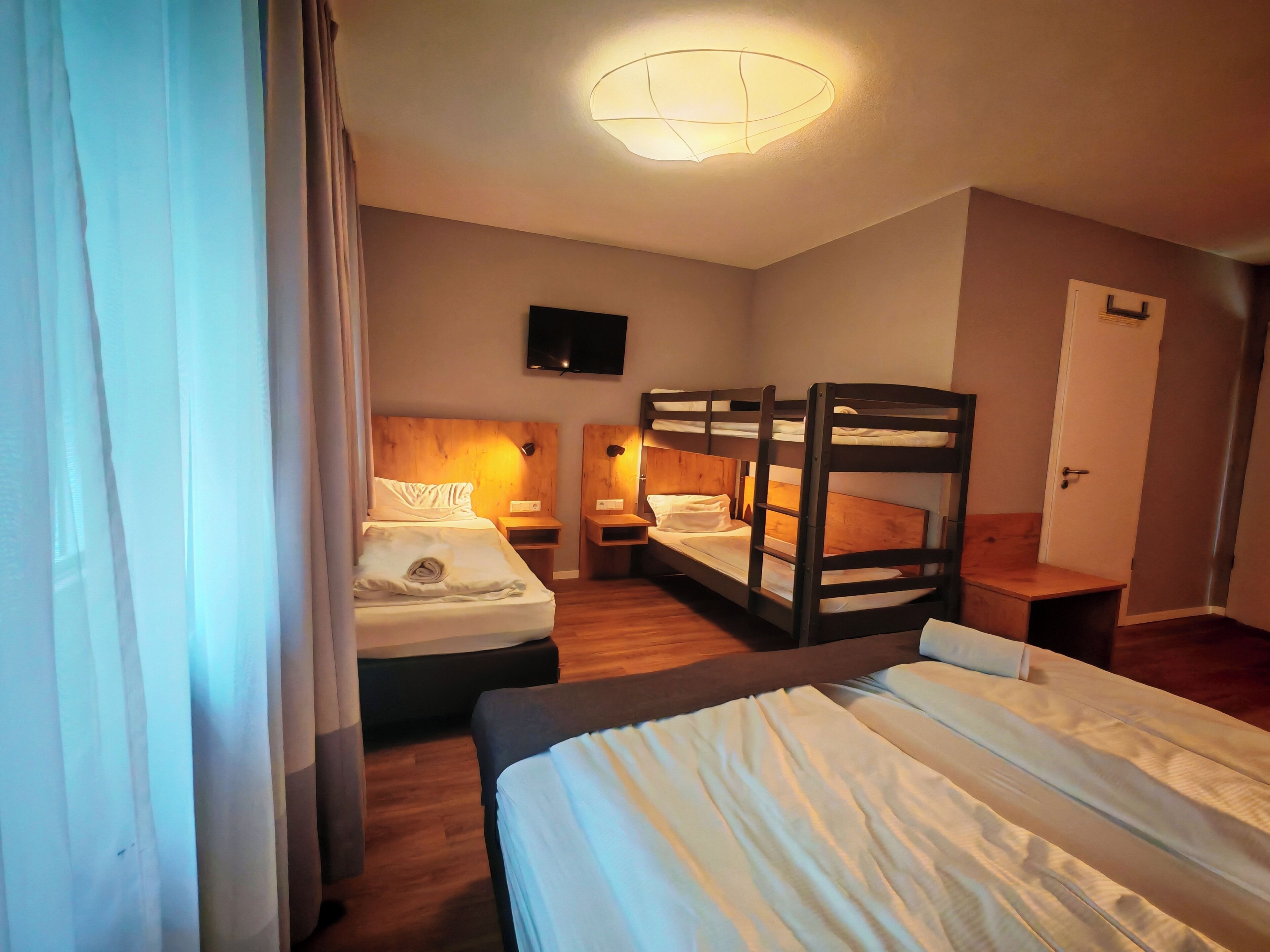 A hotel room with bunk beds, a flat-screen TV, a wooden headboard, and a bedside table with a lamp.