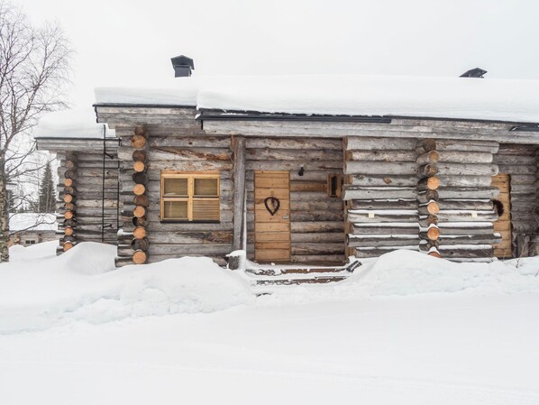 Una cabaña de troncos con puerta y ventana de madera, rodeada de nieve.