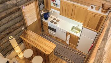 A compact kitchen with wooden cabinets, a stove, a sink, and a small dining area with stools.