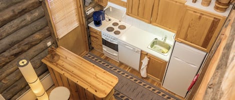 A compact kitchen with wooden cabinets, a stove, a sink, and a small dining area with stools.