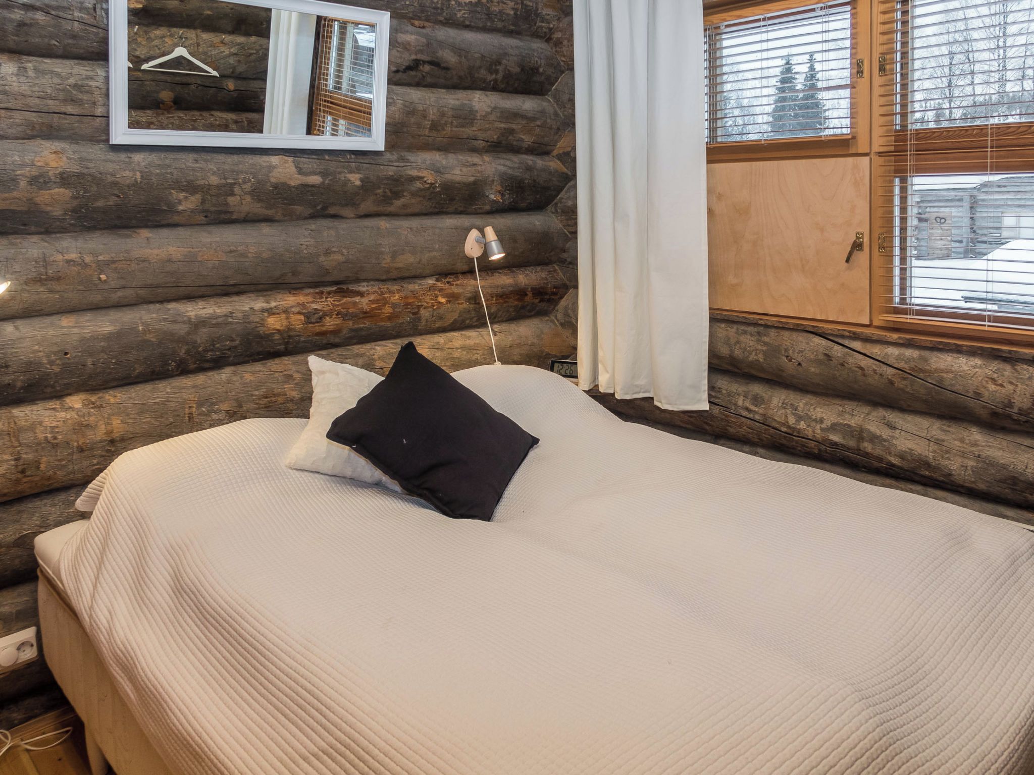 Ein Schlafzimmer in einer Blockhütte mit einem Bett, einer Hängelampe und einem Fenster mit Jalousien.