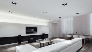 A modern living room with a white sofa, a flat-screen TV mounted on the wall, and a dining area with a wooden table and chairs. - Royal Apartment Primorskiy bulvar 1 (Odesa)