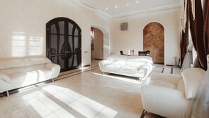 A spacious living room with a large white sofa, a smaller armchair, and a coffee table. There is a chandelier hanging from the ceiling and a large arched doorway. - Royal Apartment Uspenskaya 12 (Odesa)