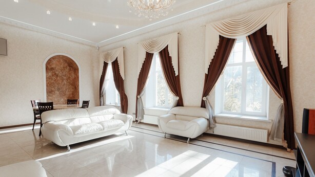 A spacious living room with a white sofa, a dining table with chairs, and large windows with brown curtains. - Royal Apartment Uspenskaya 12 (Odesa)