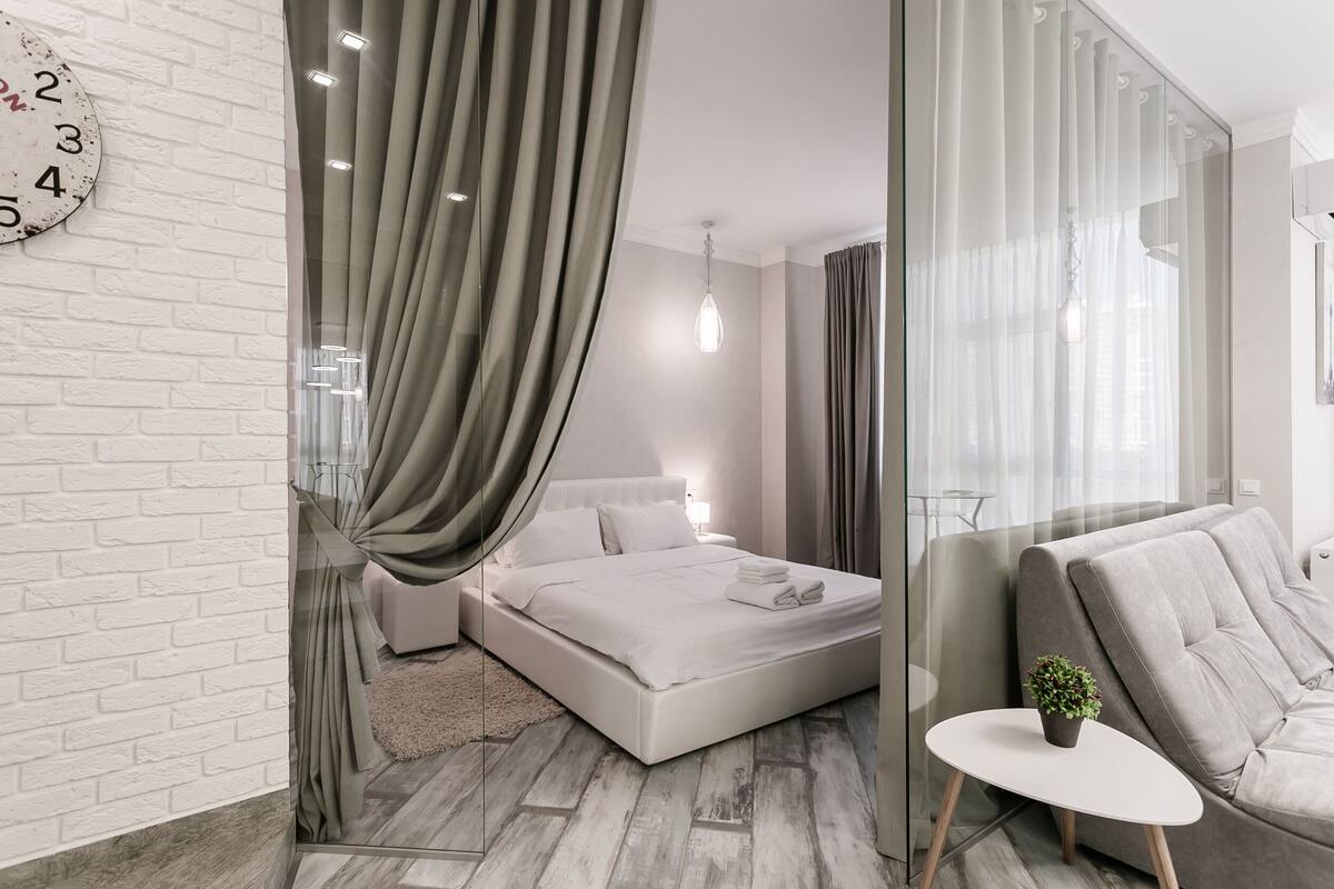 Un dormitorio moderno con una cama grande, una mesita con una planta y un panel de vidrio.