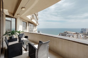 Un balcon agrémenté de meubles en osier, d’une plante en pot et offrant une vue sur la mer et le paysage urbain.
