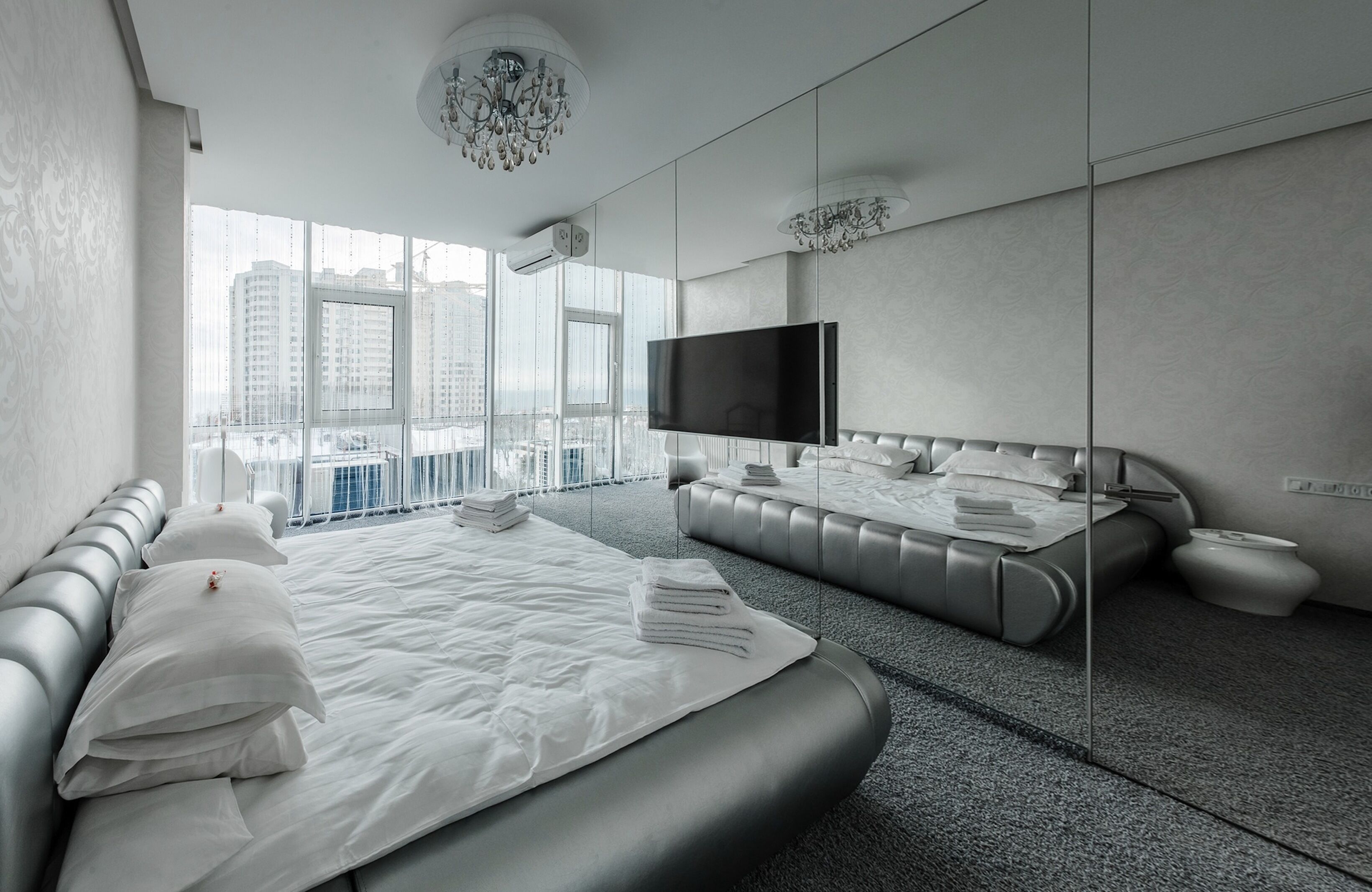 A modern hotel room with a large bed, a flat-screen TV, and a city view through large windows.