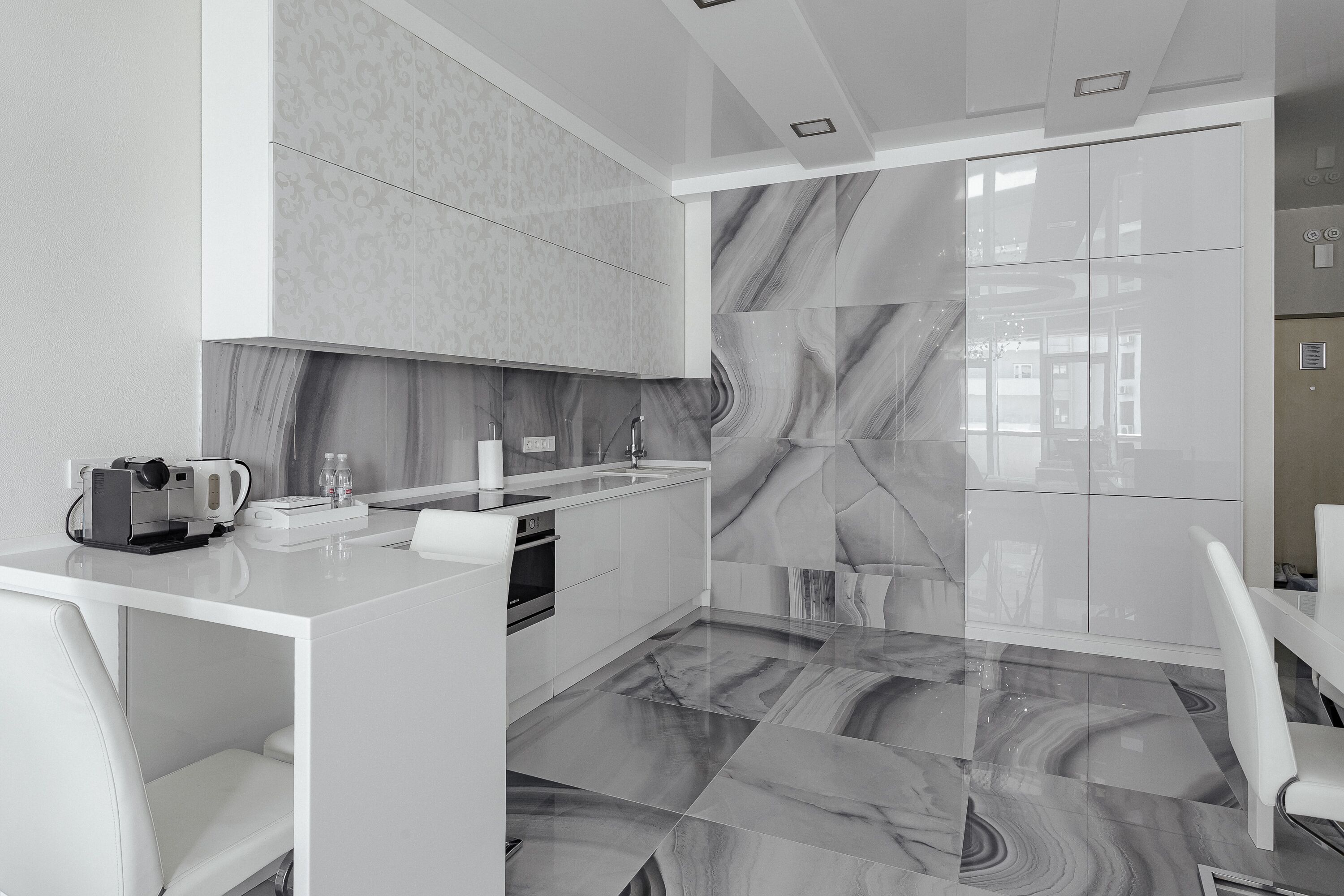 A modern kitchen with white cabinetry, a marble backsplash, and a sleek countertop.