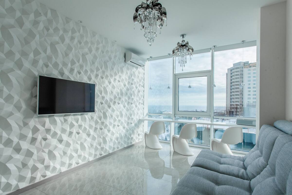 Una sala de estar moderna con un muro de diseño geométrico, un televisor de pantalla plana, un sofá gris y un balcón con vistas a la ciudad.