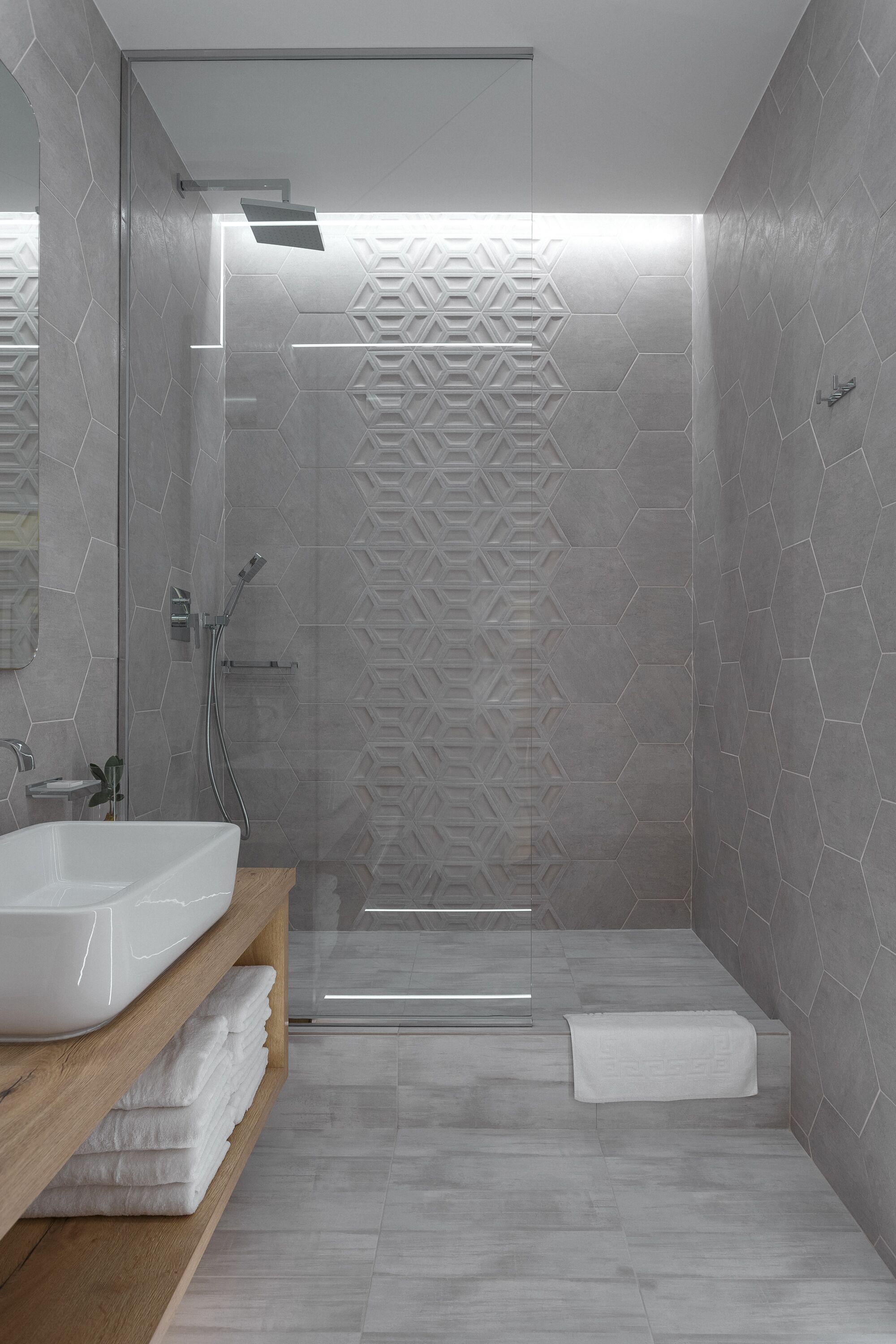 Une salle de bain moderne avec une douche à parois de verre, un lavabo blanc et une étagère en bois où sont posées des serviettes.
