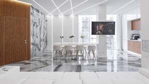 Une cuisine moderne avec un plan de travail en marbre, un coin repas avec des chaises blanches et un grand téléviseur fixé au mur.