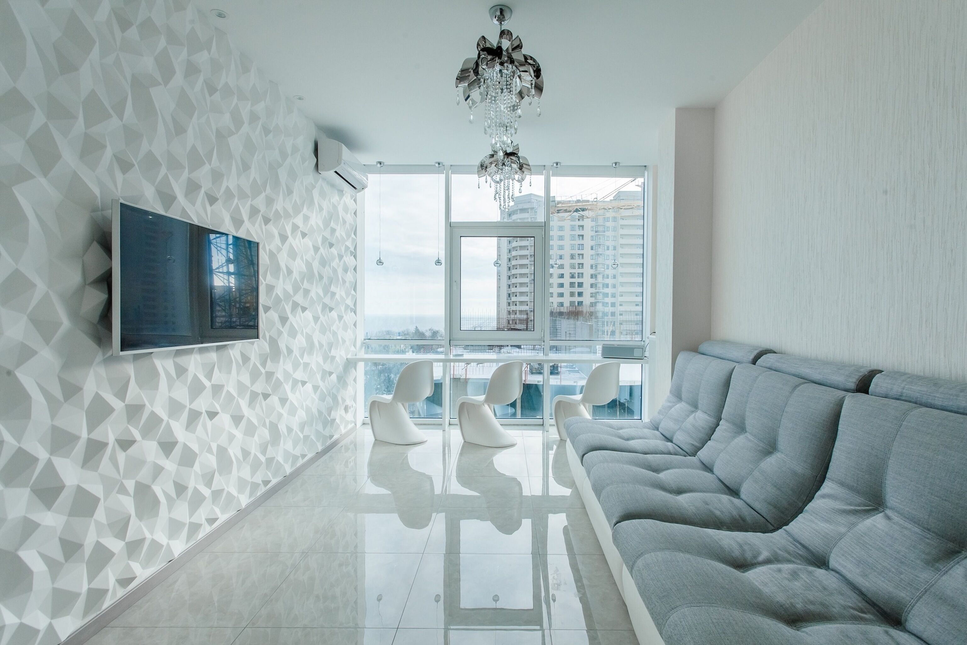 Un salon moderne avec un motif géométrique sur le mur, un grand téléviseur à écran plat, un canapé gris et un lustre.