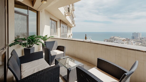 Un balcon agrémenté de meubles en osier, d’une table en verre et d’une plante en pot.