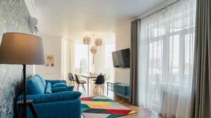 A modern living room with a blue sofa, a lamp, a colorful rug, and a dining area with chairs and a table. - Royal Apartment Zhukovskogo 9 (Odesa)