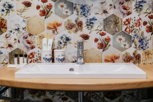 Un baño con lavamanos blanco, un espejo y un salpicadero de azulejos hexagonales con diseño floral.