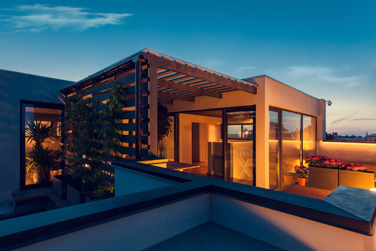 A modern rooftop terrace with a pergola, glass doors, and potted plants.