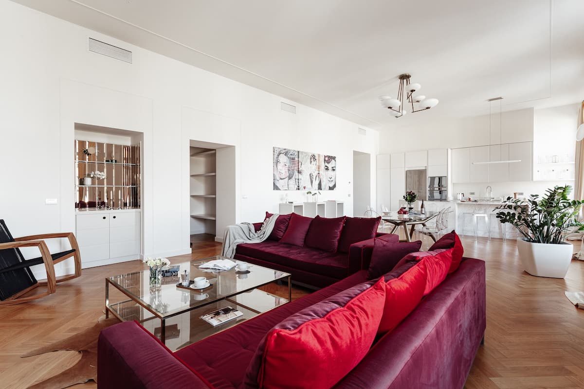 A modern living room with a red sofa, a glass coffee table, and a dining area with a white table and chairs.