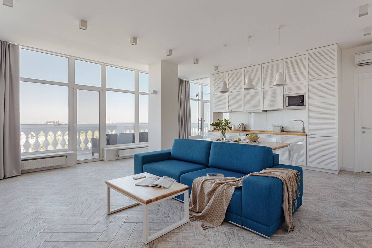 A modern living room with a blue sofa, a wooden coffee table, and a view of the city through large windows.