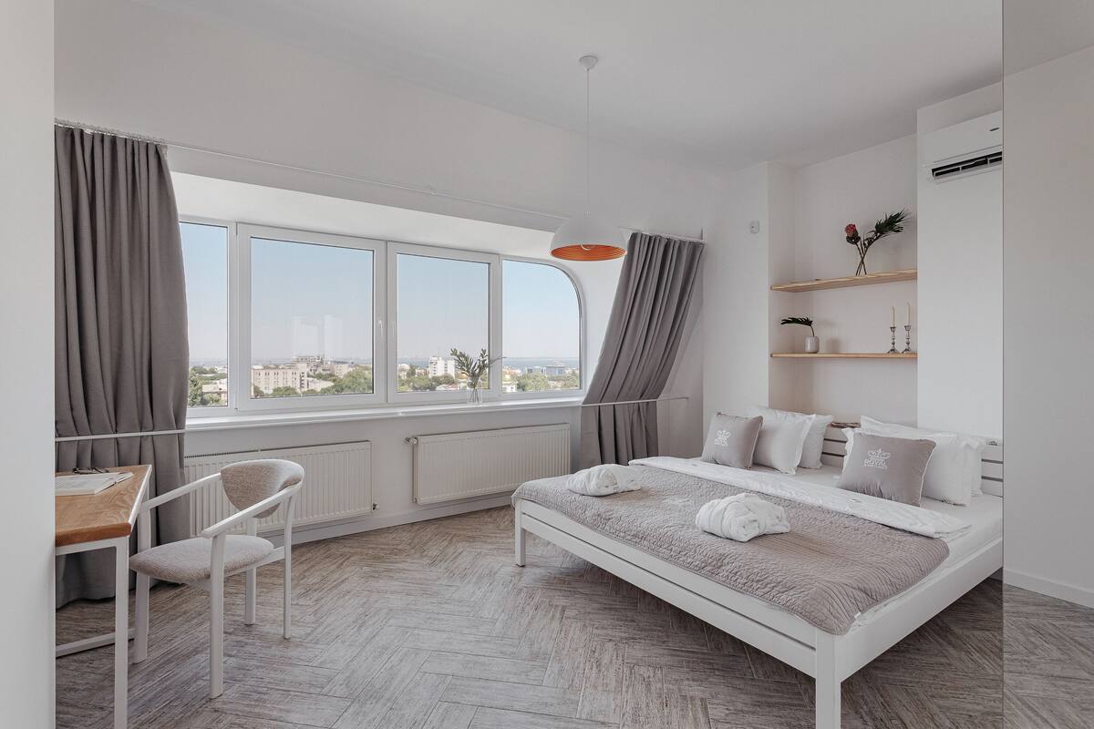 A modern bedroom with a large window, a bed, a desk, and a chair.