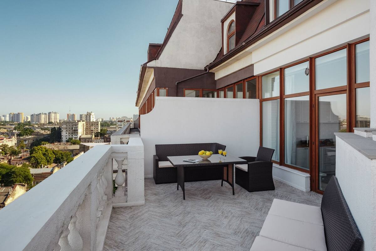 A balcony with a sofa, table, and chairs, overlooking a cityscape.