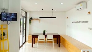 A modern, well-lit room with a dining table, two chairs, a mounted TV, and a wall-mounted shelf with plants.