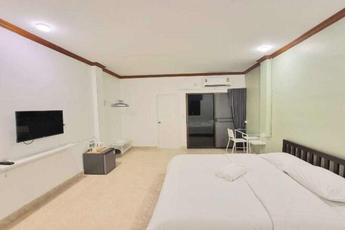 A hotel room with a bed, a desk, a chair, a television, and an air conditioning unit.