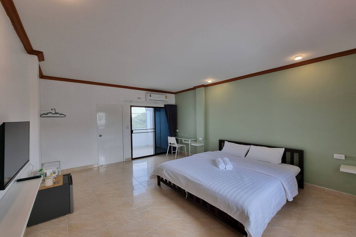 A hotel room with a bed, a desk, a chair, a TV, and an air conditioning unit.