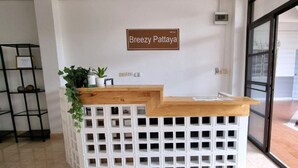 A reception desk with a wooden top and a white, grid-patterned base. A sign above reads "Breezy Pattaya."