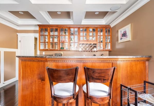A kitchen with wooden cabinets, a central island with chairs, and a white door in the background.