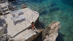 Una plataforma de piedra con sillones de descanso y una escalera que lleva a aguas azules cristalinas.