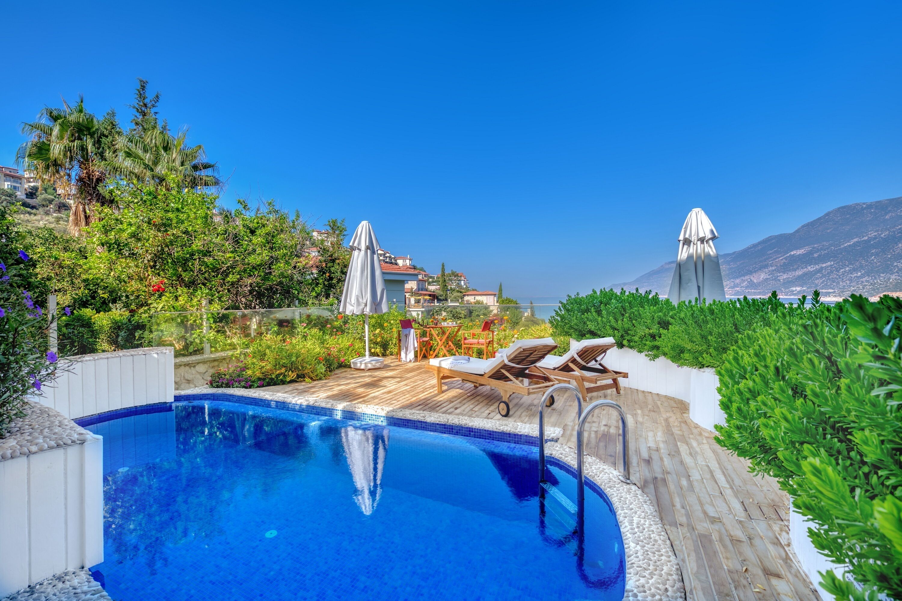 Zona de piscina amb gandules, ombrel·les i vista a edificis i muntanyes.