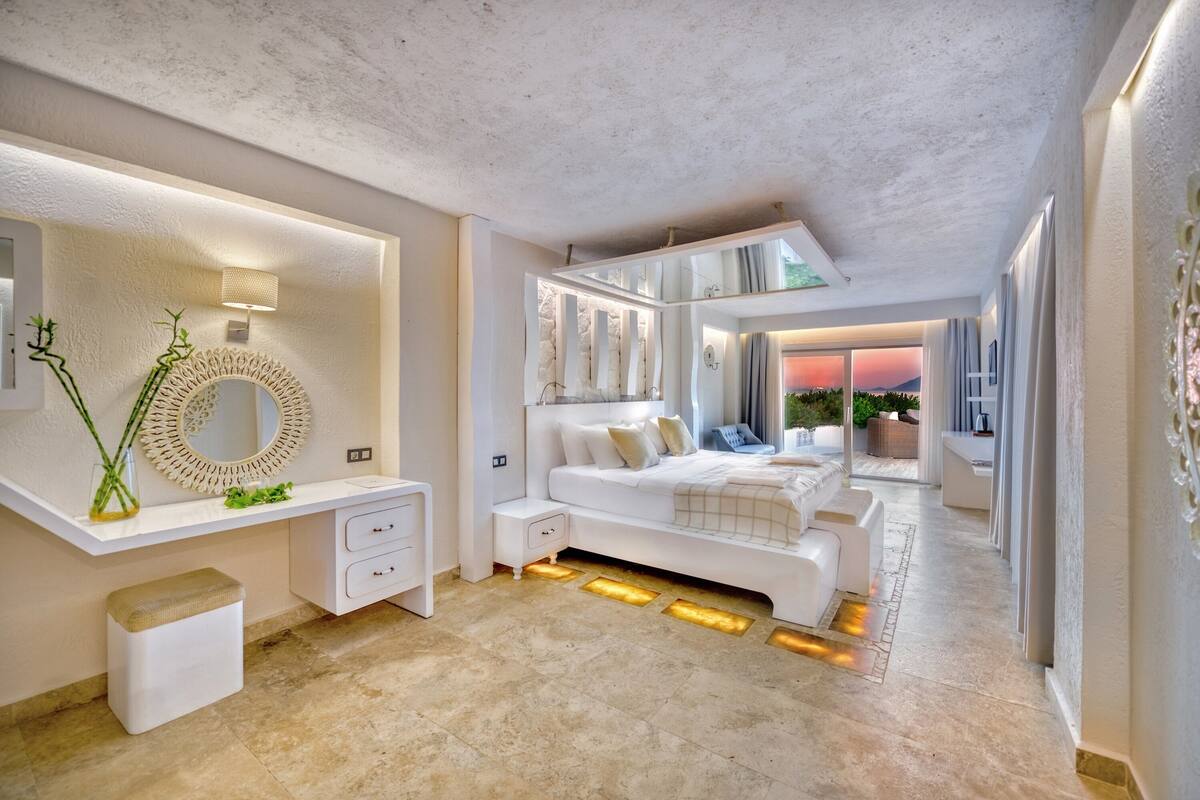 A modern bedroom with a large bed, a vanity with a mirror, and a view of the outdoors.