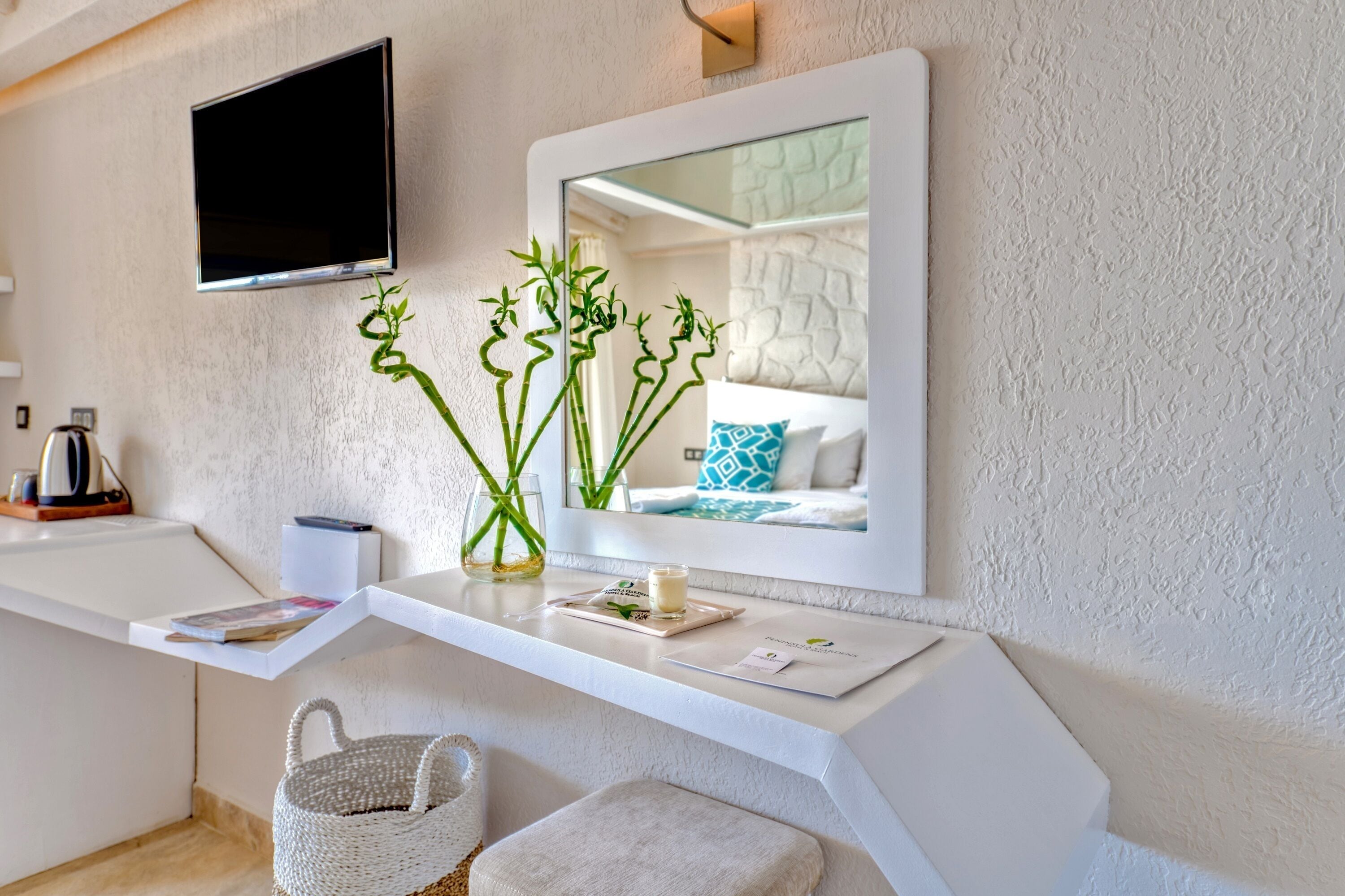 A modern bathroom with a white vanity, a mounted TV, a mirror, and a vase with green plants.